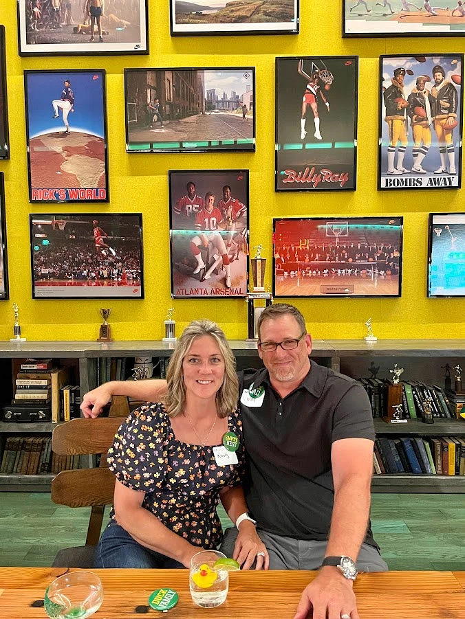 A couple sits together at a table in front of a wall decorated with various sports-themed posters and memorabilia.